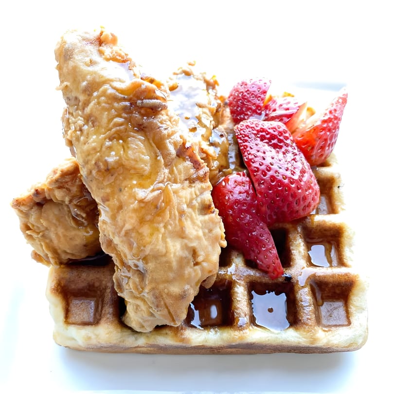 Golden fried chicken and fresh strawberries drizzled with syrup on a waffle.
