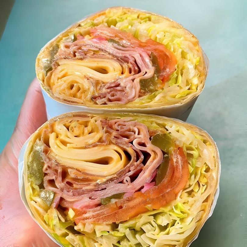 A Taps Valley Gastropub wrap, cut in half, revealing layers of meat, cheese, lettuce, and pickles.