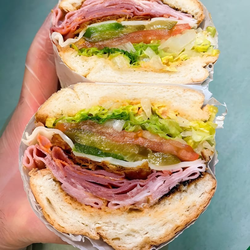 A large Taps Valley Gastropub sub sandwich, cut in half, revealing layers of meat, cheese, and vegetables.