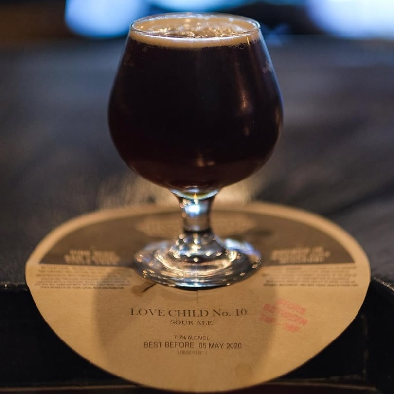 Dark sour ale in a stemmed glass with a foamy head, on a coaster at Taps Valley Gastropub.