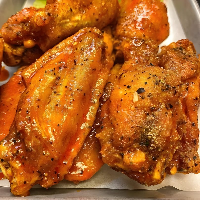 Close-up of several Taps Valley Gastropub chicken wings, coated in a glossy orange sauce and black pepper.