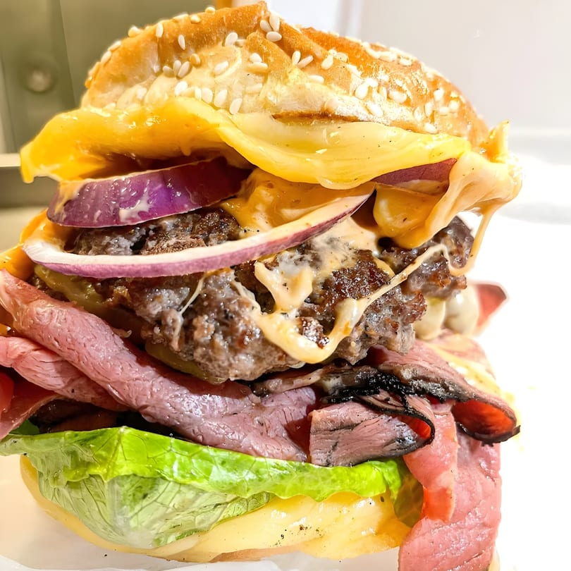 A towering Taps Valley Gastropub burger with double patties, roast beef, cheese, red onion, and lettuce.