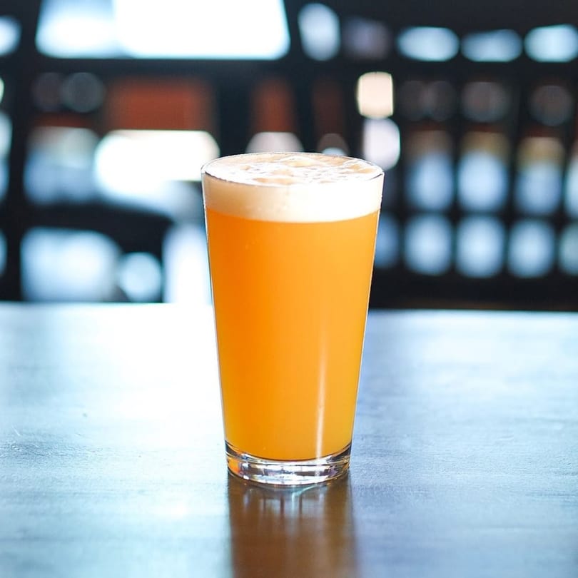 A pint glass of Taps Valley Gastropub's golden beer with a foamy head on a dark table.